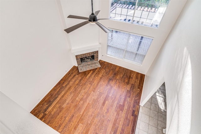 unfurnished living room with ceiling fan, wood finished floors, a high ceiling, and a fireplace