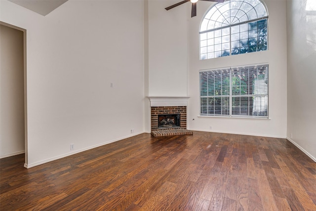 unfurnished living room with ceiling fan, wood finished floors, a towering ceiling, a fireplace, and baseboards