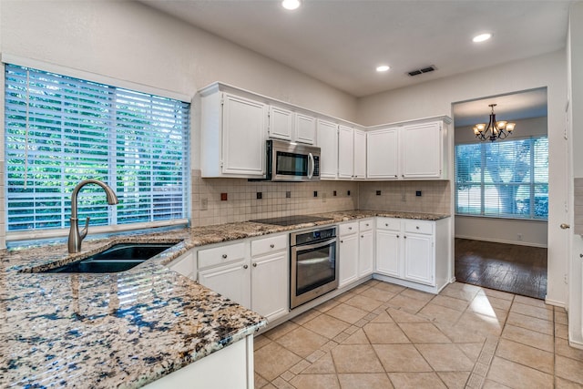 kitchen with appliances with stainless steel finishes, a sink, tasteful backsplash, a chandelier, and light tile patterned floors