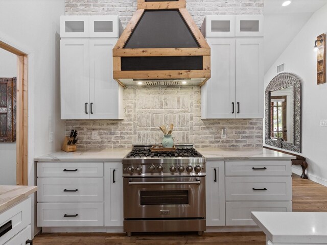 kitchen with high end stainless steel range oven, custom range hood, white cabinetry, decorative backsplash, and glass insert cabinets
