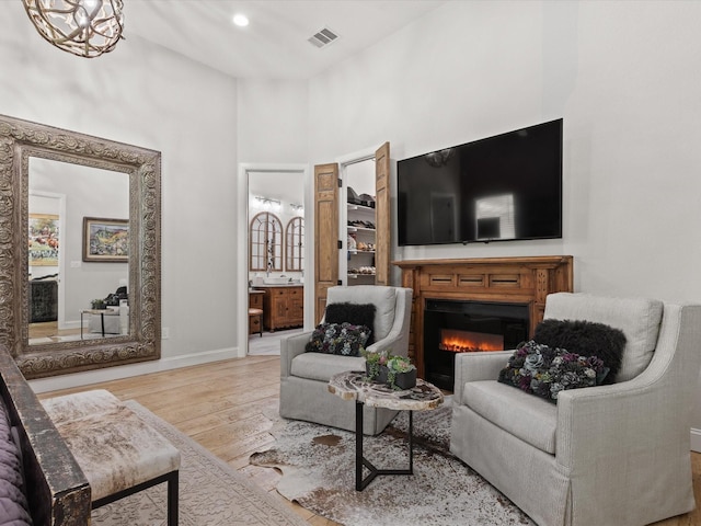 living room featuring wood finished floors, a towering ceiling, a glass covered fireplace, and baseboards