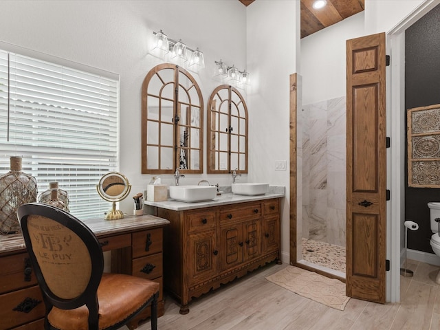 bathroom with tiled shower, toilet, double vanity, and wood finished floors