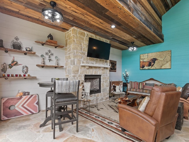 living room featuring wood walls, wood ceiling, stone finish flooring, and an outdoor stone fireplace