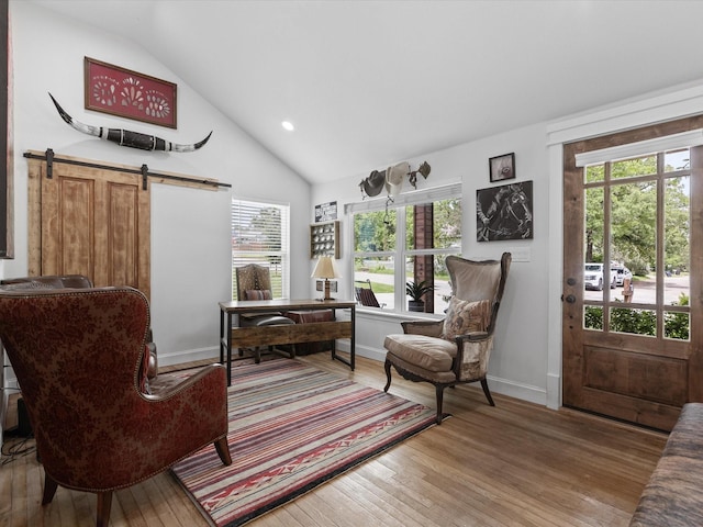 living area featuring vaulted ceiling, light wood-style flooring, healthy amount of natural light, a barn door, and baseboards