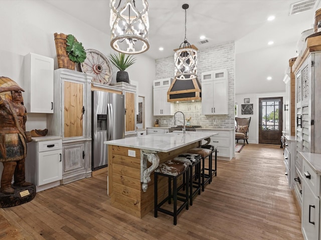 kitchen featuring stainless steel fridge, wood finished floors, an island with sink, a breakfast bar, and glass insert cabinets
