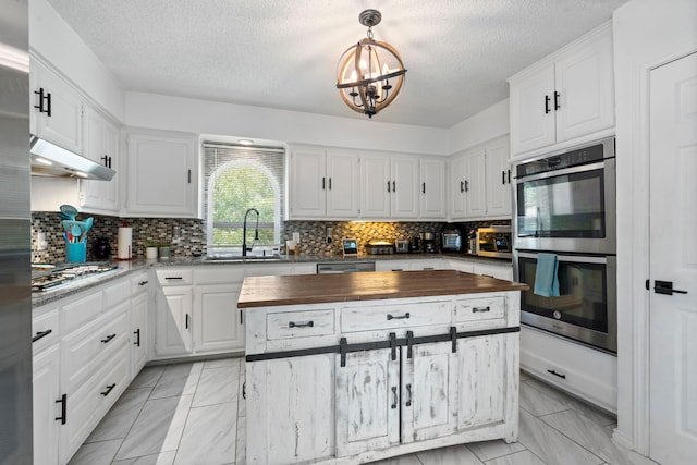 1426 Northridge Dr, Carrollton, TX 75006 - kitchen featuring butcher block counters, a sink, appliances with stainless steel finishes, under cabinet range hood, and a chandelier