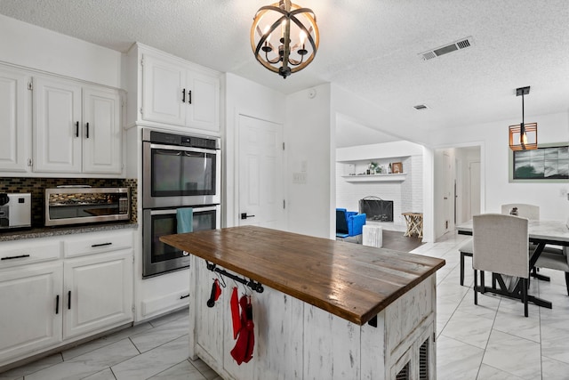 1426 Northridge Dr, Carrollton, TX 75006 - kitchen featuring butcher block countertops, light marble finish flooring, a brick fireplace, appliances with stainless steel finishes, and a textured ceiling