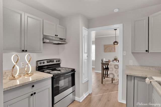 kitchen with electric range, under cabinet range hood, light wood finished floors, baseboards, and light stone counters