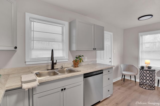 kitchen featuring stainless steel dishwasher, a sink, light wood-type flooring, light countertops, and plenty of natural light
