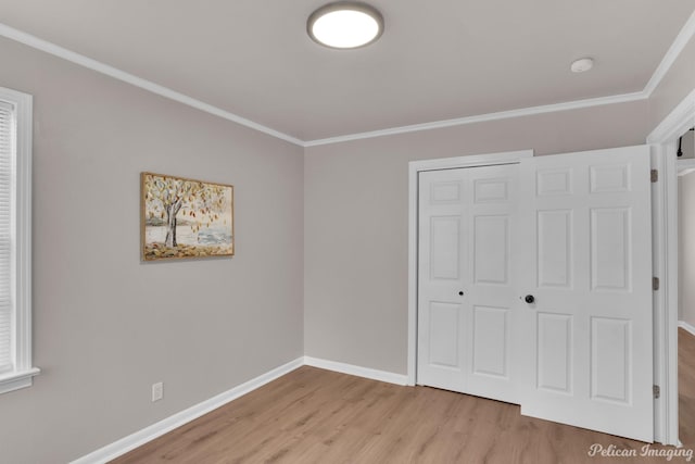 unfurnished bedroom featuring light wood-style floors, crown molding, baseboards, and a closet