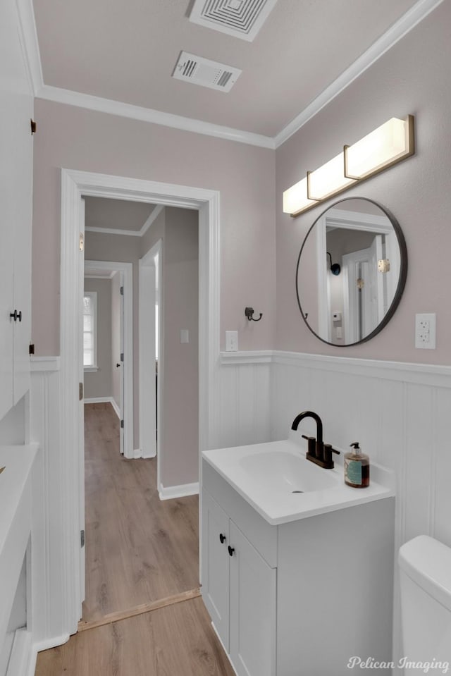 bathroom with wood finished floors, toilet, vanity, ornamental molding, and a wainscoted wall
