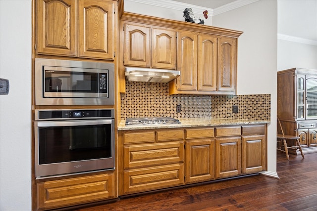 kitchen with appliances with stainless steel finishes, under cabinet range hood, backsplash, dark wood-style floors, and ornamental molding