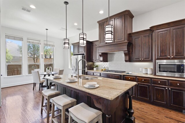 901 Clear Water Dr, Allen, TX 75013 - kitchen with stainless steel appliances, a sink, decorative backsplash, a breakfast bar area, and dark brown cabinetry