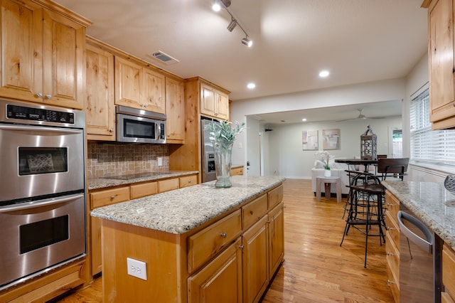 5820 Forest Ln, Dallas, TX 75230 - kitchen with appliances with stainless steel finishes, a kitchen island, light wood finished floors, backsplash, and light stone countertops