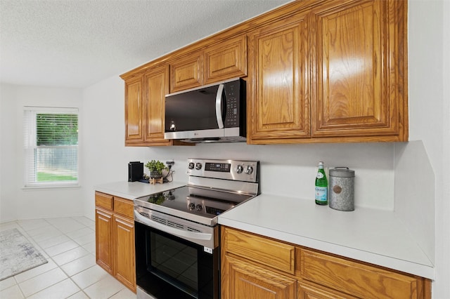 218 Whispering Dell Ln, Weatherford, TX 76085 - kitchen featuring stainless steel appliances, brown cabinetry, light countertops, light tile patterned floors, and a textured ceiling