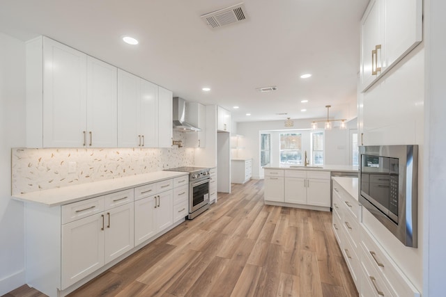 2815 Perkins Rd, Arlington, TX 76016 - kitchen featuring appliances with stainless steel finishes, wall chimney exhaust hood, a sink, a peninsula, and light wood-style floors