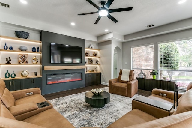 living room with ceiling fan, wood finished floors, a glass covered fireplace, arched walkways, and recessed lighting