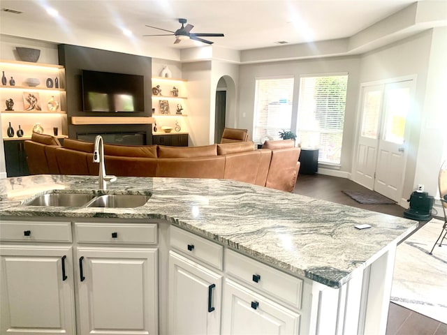 kitchen featuring a sink, ceiling fan, arched walkways, white cabinetry, and light stone counters
