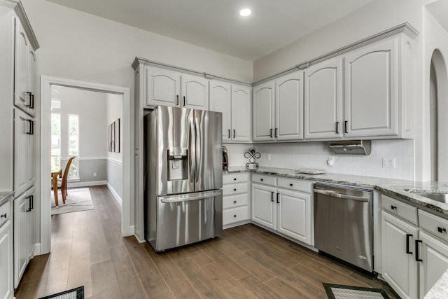 kitchen featuring appliances with stainless steel finishes, light stone counters, dark wood-type flooring, backsplash, and white cabinets