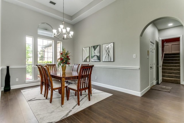 dining space featuring arched walkways, stairway, a chandelier, dark wood-type flooring, and baseboards