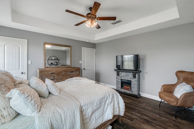 160 Grays Creek Cir, Alma, TX 75119 - bedroom with a tray ceiling, baseboards, dark wood-style floors, a stone fireplace, and a ceiling fan
