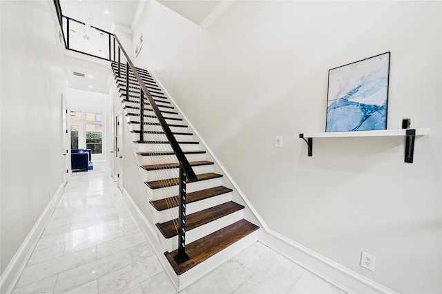 staircase with marble look tiles, baseboards, and a towering ceiling