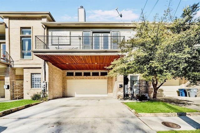 view of front of home featuring a balcony, brick siding, an attached garage, concrete driveway, and a chimney