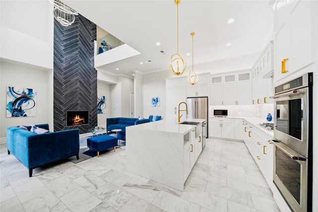 kitchen featuring stainless steel double oven, light marble finish floors, open floor plan, gas stovetop, and light stone counters