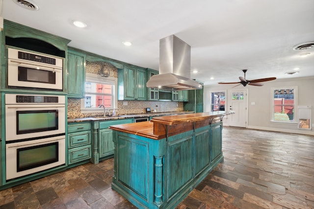 kitchen featuring green cabinetry, island range hood, butcher block countertops, white double oven, and decorative backsplash