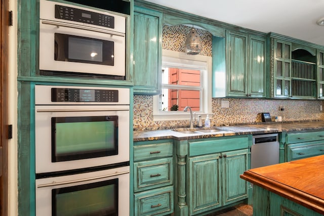 kitchen featuring green cabinetry, a sink, double oven, and decorative backsplash