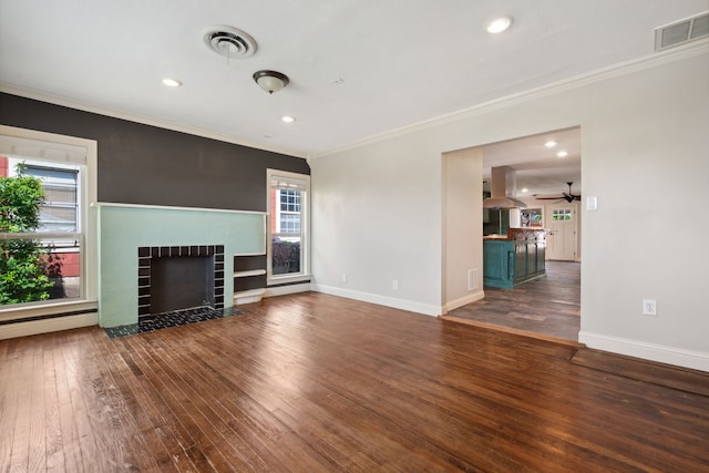 unfurnished living room with wood-type flooring, a tile fireplace, crown molding, ceiling fan, and baseboards