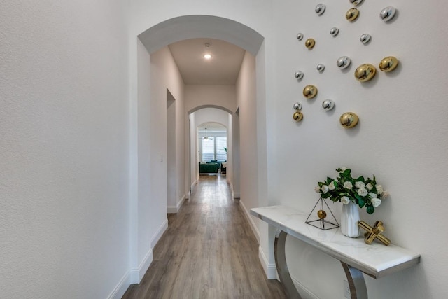 corridor with arched walkways, wood finished floors, and baseboards