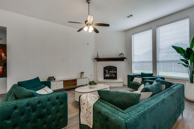 living room with healthy amount of natural light, wood finished floors, a ceiling fan, and a brick fireplace