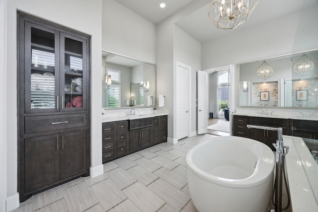 bathroom with a chandelier, a soaking tub, two vanities, and baseboards