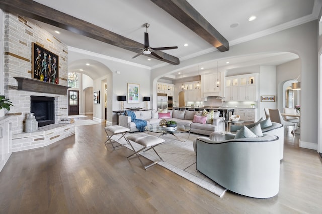 living area featuring arched walkways, beam ceiling, wood finished floors, a ceiling fan, and recessed lighting