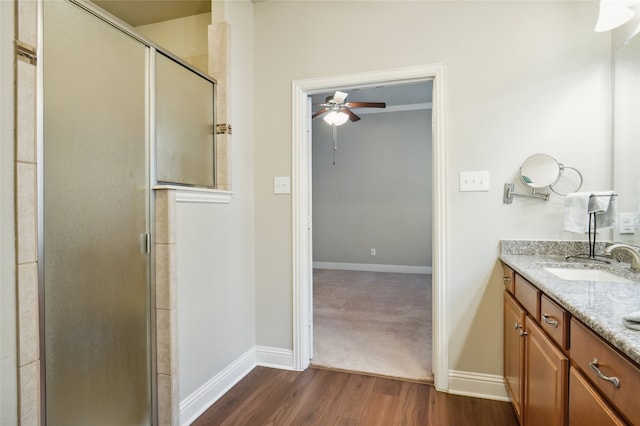 full bath with a ceiling fan, wood finished floors, a stall shower, vanity, and baseboards