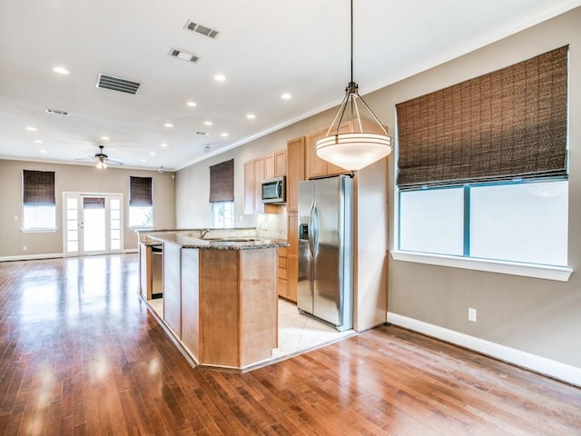 kitchen featuring appliances with stainless steel finishes, baseboards, crown molding, a center island with sink, and ceiling fan