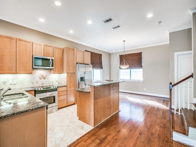 kitchen featuring appliances with stainless steel finishes, a sink, crown molding, a kitchen island, and stone countertops