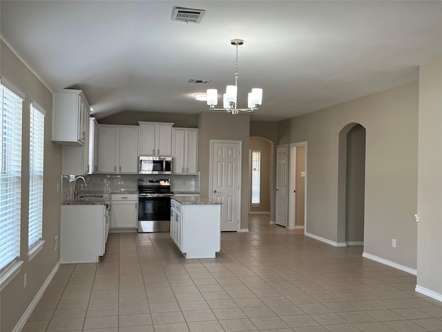 3108 Bryce Dr, Wylie, TX 75098 - kitchen featuring appliances with stainless steel finishes, arched walkways, backsplash, light tile patterned floors, and vaulted ceiling