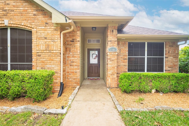 entrance to property with brick siding and a shingled roof