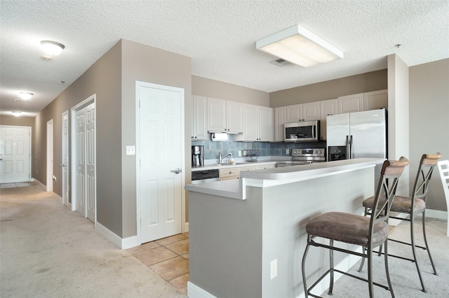 kitchen with appliances with stainless steel finishes, a kitchen bar, a sink, light carpet, and light countertops