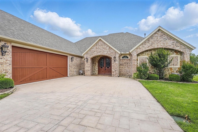 9008 Reata W Dr, Benbrook, TX 76126 - french country home with roof with shingles, a garage, decorative driveway, a front lawn, and brick siding