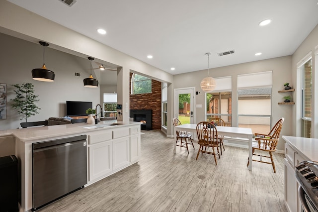 kitchen with a sink, appliances with stainless steel finishes, a glass covered fireplace, light countertops, and light wood-style floors
