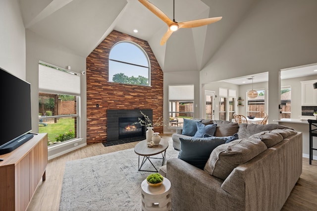 living area with high vaulted ceiling, a fireplace with flush hearth, healthy amount of natural light, and light wood-style floors
