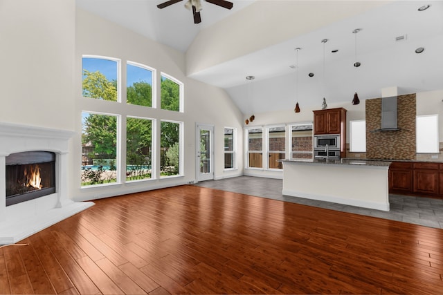 8204 Saint Clair Dr, Mckinney, TX 75071 - unfurnished living room with high vaulted ceiling, a warm lit fireplace, a ceiling fan, and light wood-style flooring
