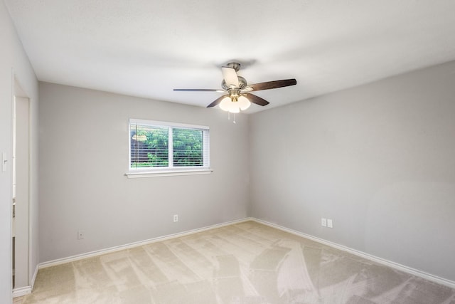 spare room featuring light colored carpet, ceiling fan, and baseboards