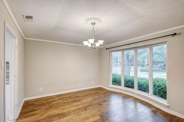 empty room featuring a chandelier, wood finished floors, crown molding, baseboards, and a textured ceiling