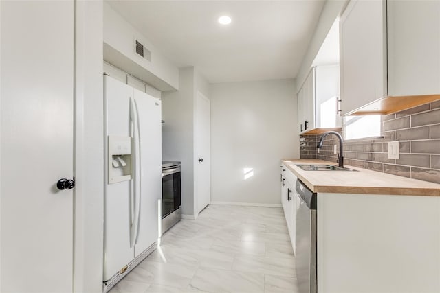 323 Towne House Ln, Richardson, TX 75081 - kitchen featuring appliances with stainless steel finishes, a sink, light marble finish flooring, white cabinets, and backsplash