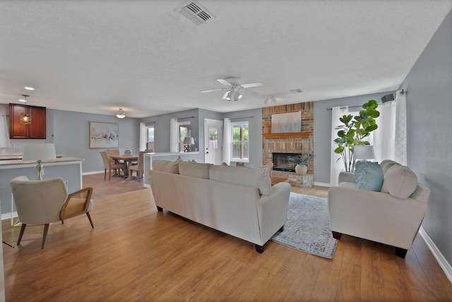 2200 Bantry Ln, Arlington, TX 76002 - living room with a textured ceiling, a fireplace, baseboards, light wood-style flooring, and ceiling fan