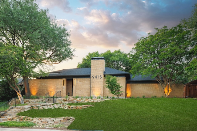 9415 Hill View Dr, Dallas, TX 75231 - back of house at dusk featuring a chimney, brick siding, and a shingled roof
